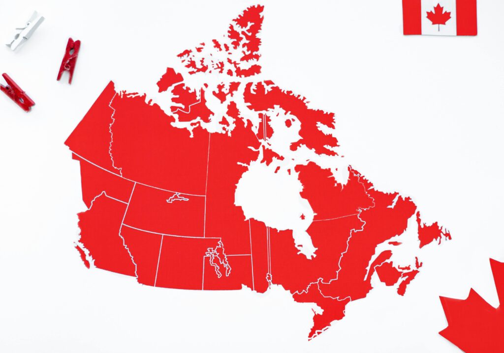 A red map of Canada with flag accents and decorative clothespins on a white background.